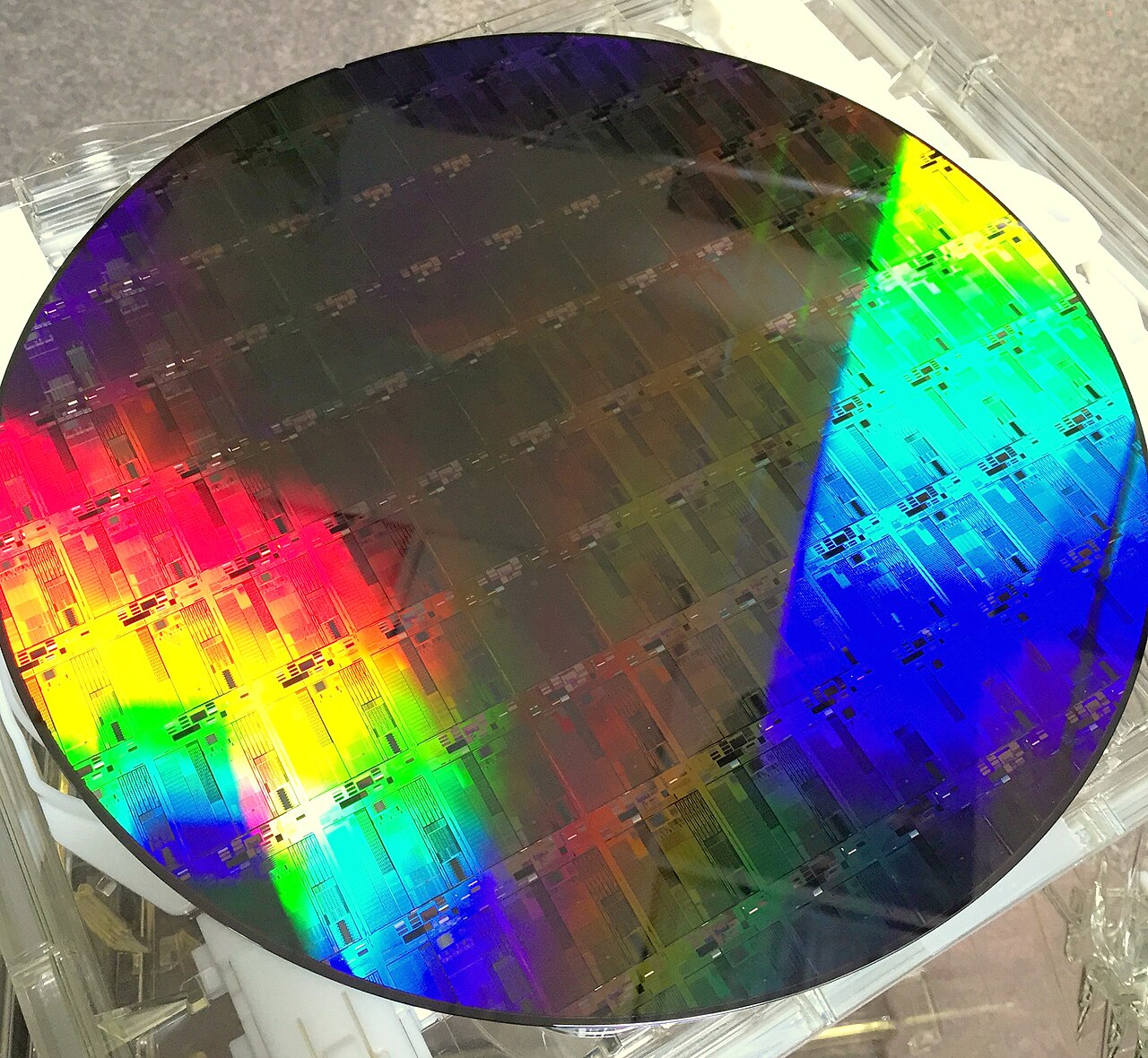 A 300-millimetre silicon wafer held at an angle, its surface refracting light into bands of colour.