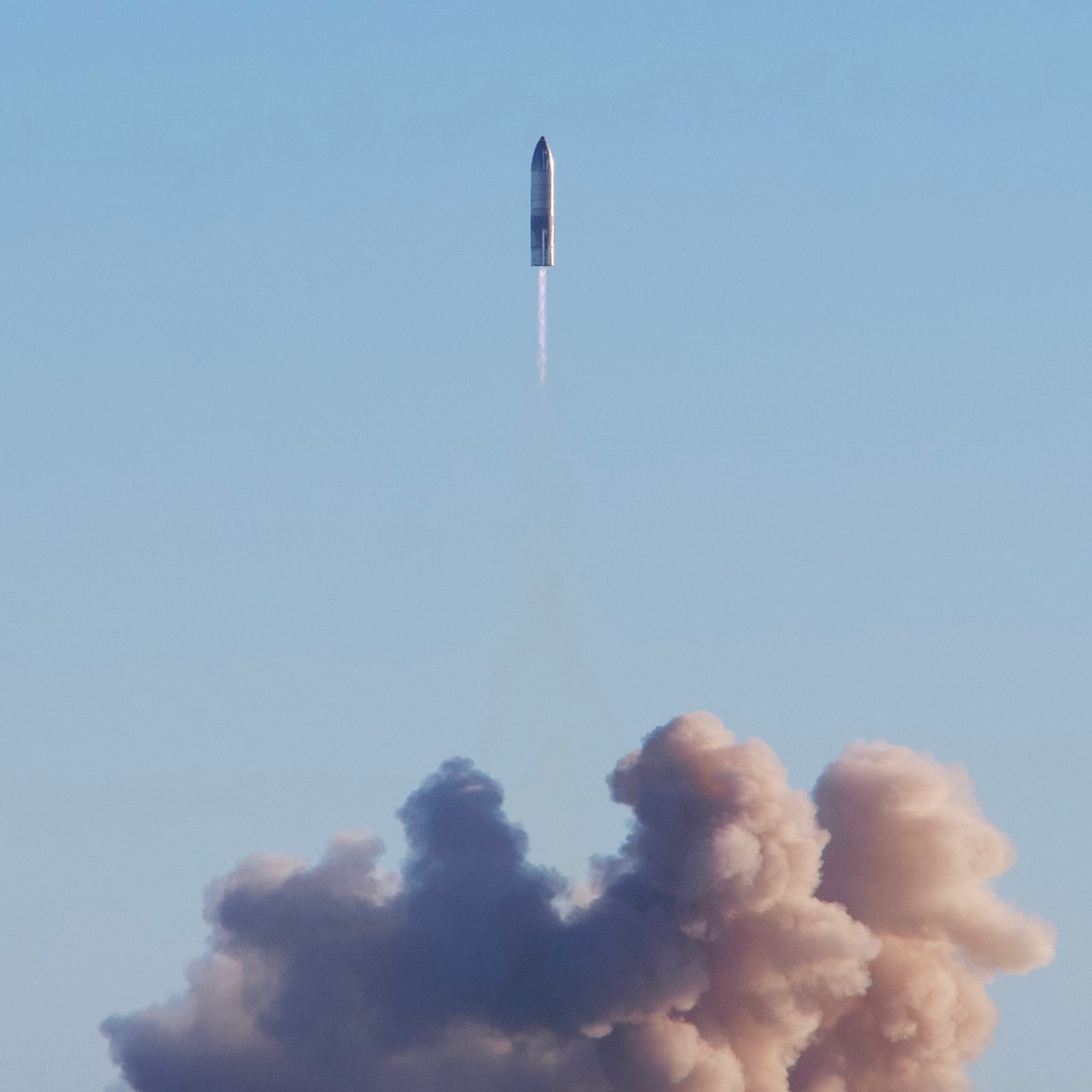 A SpaceX Starship prototype rising on a column of engine exhaust against a clear sky.